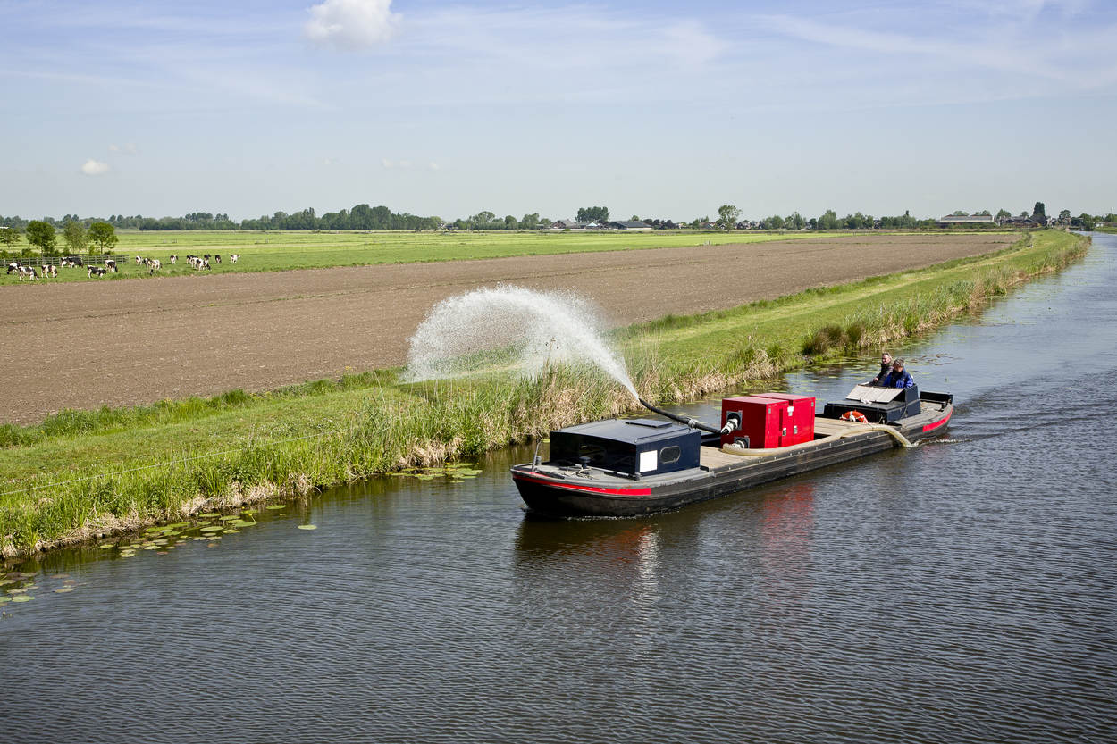 Vanuit een bootje wordt het gras op de kade gesproeid