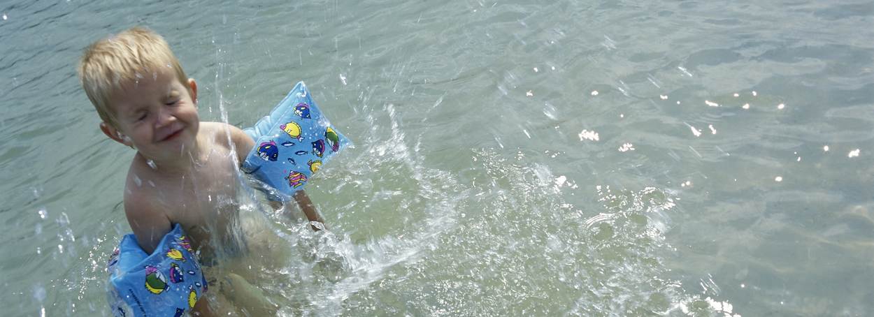 Een jongetje met zwembandjes om speelt in het water