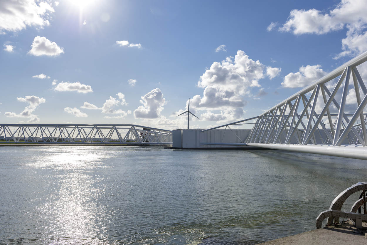 Een metalen constructie boven water, op de achtergrond zie je een windmolen