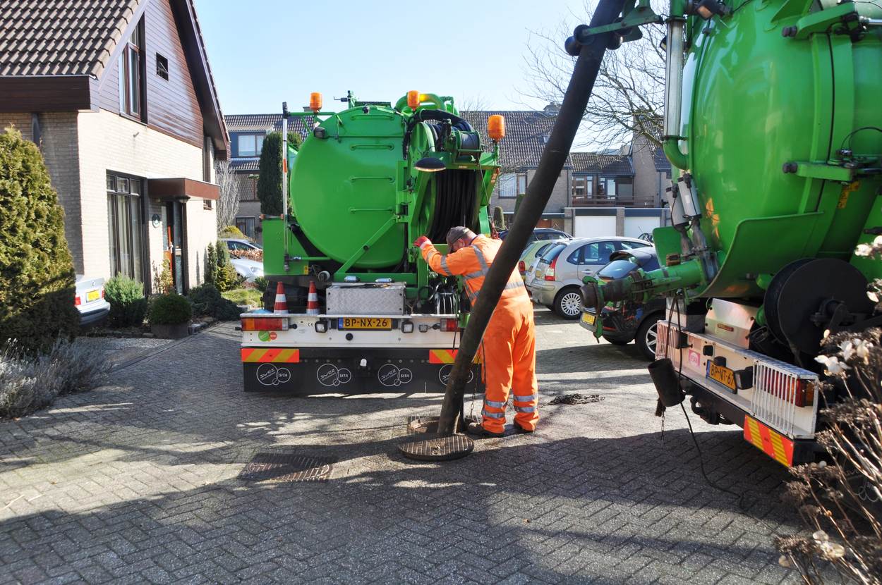 Een man reinigt met een rioolreinigingswagen het riool