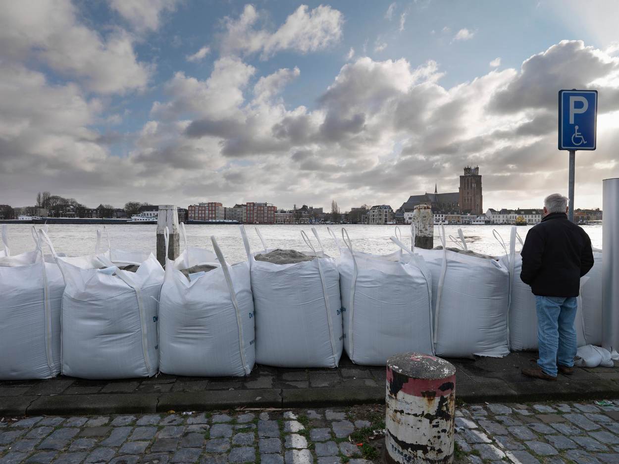 Een man staat naast zandzakken die bij een kanaal op een parkeerplaats staan