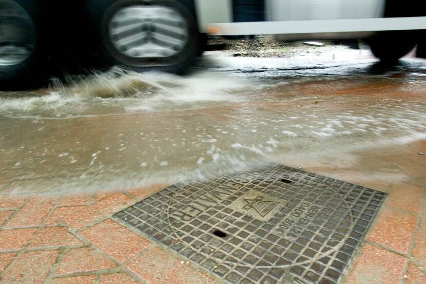 Een vrachtwagen rijdt langs een put door een grote plas water.