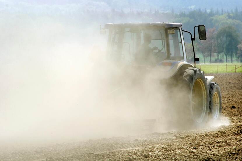 Een tractor met een stofwolk erachter rijdt over omgeploegde landbouwgrond.