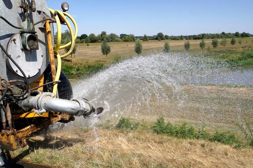 Een sproeimachine sproeit water over dor gras.