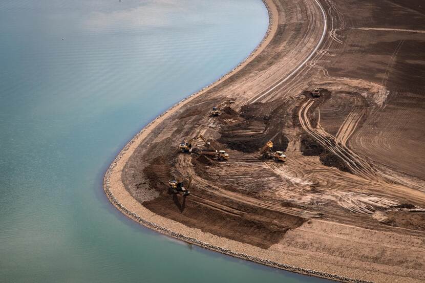 Luchtfoto van graafmachines die langs de oever van de Maas aan het werk zijn.