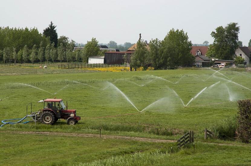 Stuk weiland wordt op verschillende plekken besproeid met waterinstallaties terwijl een tractor langs rijdt