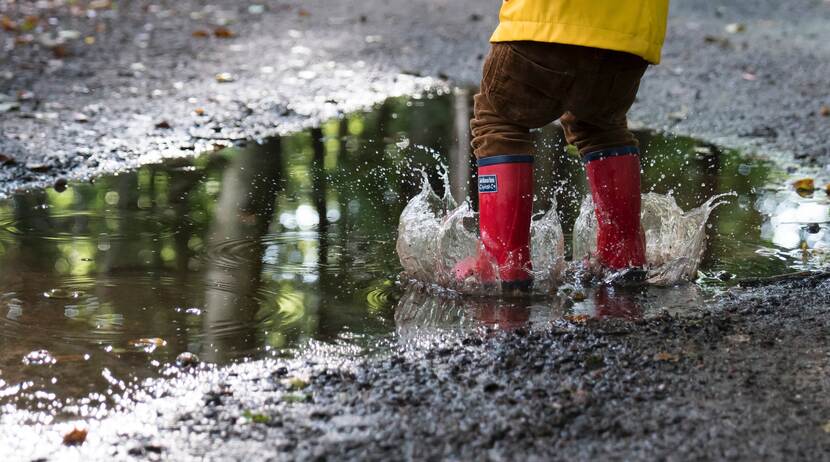 kind met regenlaarzen in plas