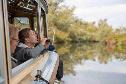 vrouw kijkt naar buiten met verrekijker vanuit boot