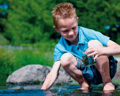 Kind onderzoekt water met potje in hand